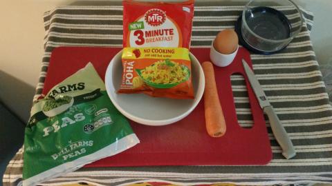 Ingredients on a chopping board. A bag of frozen peas, a carrot, an egg, and a bag of Indian-style 3-minute rice.