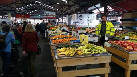 A produce stall with a rather glum-looking stallholder in a high-vis jacket staring into space.