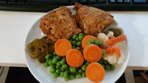 A small plate with two pieces of fried chicken and vegetable accompaniments.