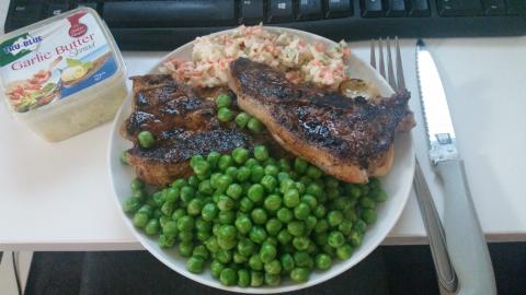 A small plate with a big lamb chop, cut in half, served with coleslaw and too many peas.