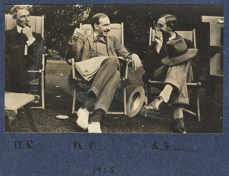 Bertrand Russell, J.M. Keynes, and Lytton Strachey seated in lawn chairs, the latter two in animated conversation while Russell draws on his pipe and looks on in amusement.