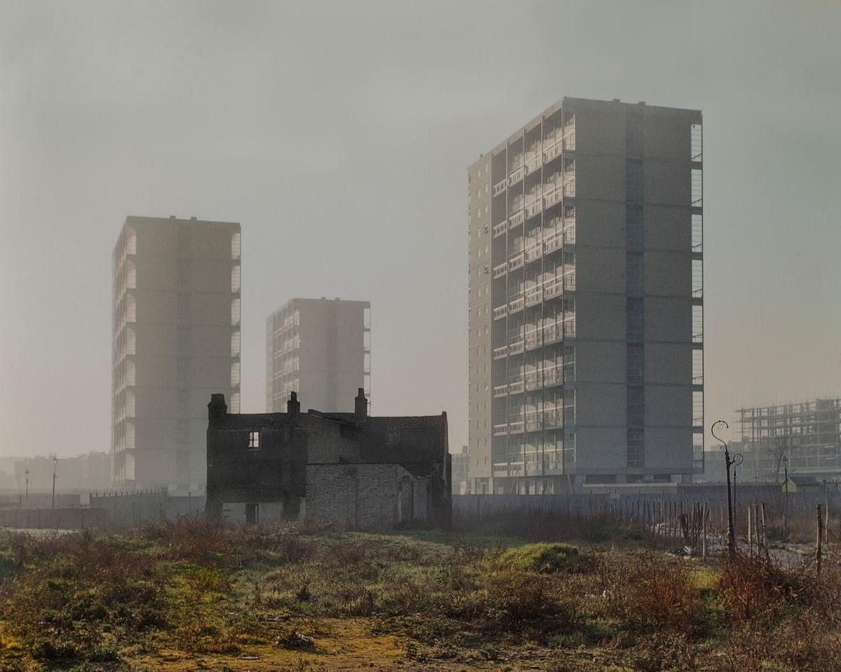 A row of three derelict terrace house facades in the foreground of three looming modernist residential tower blocks.