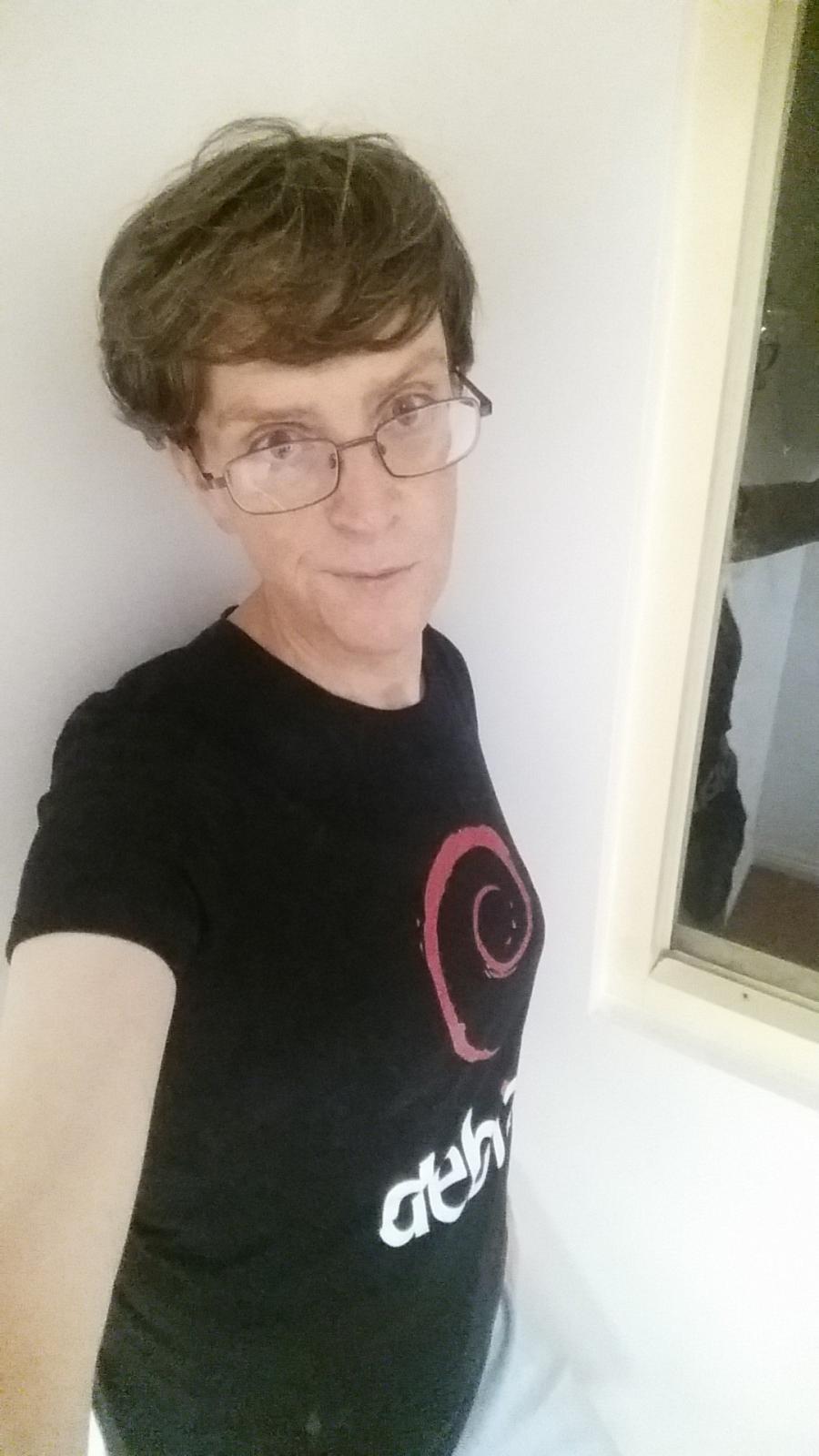 Old lady taking a selfie in the stairwell of a run-down apartment building. No makeup, wearing a Debian T-shirt.