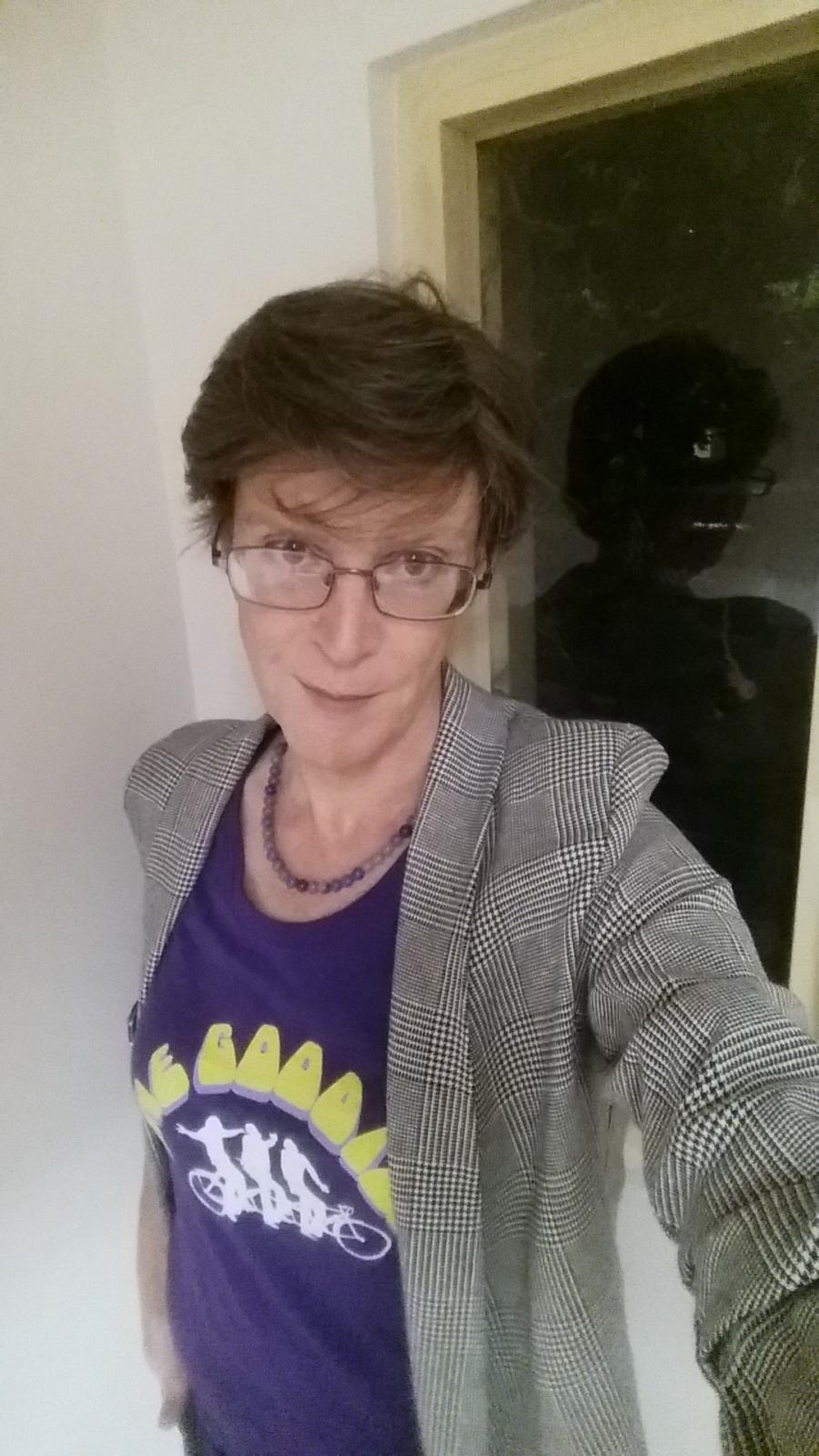 Old lady taking a selfie in the stairwell of a run-down apartment building. Light makeup, wearing a Goodies t-shirt.