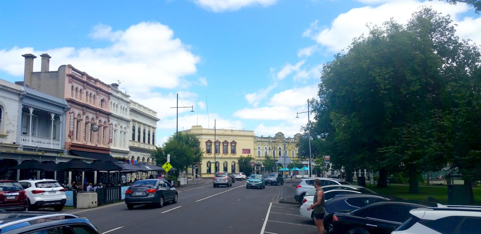 A row of old buildings, mainly restaurants, along the main street of a suburb, opposite a park.