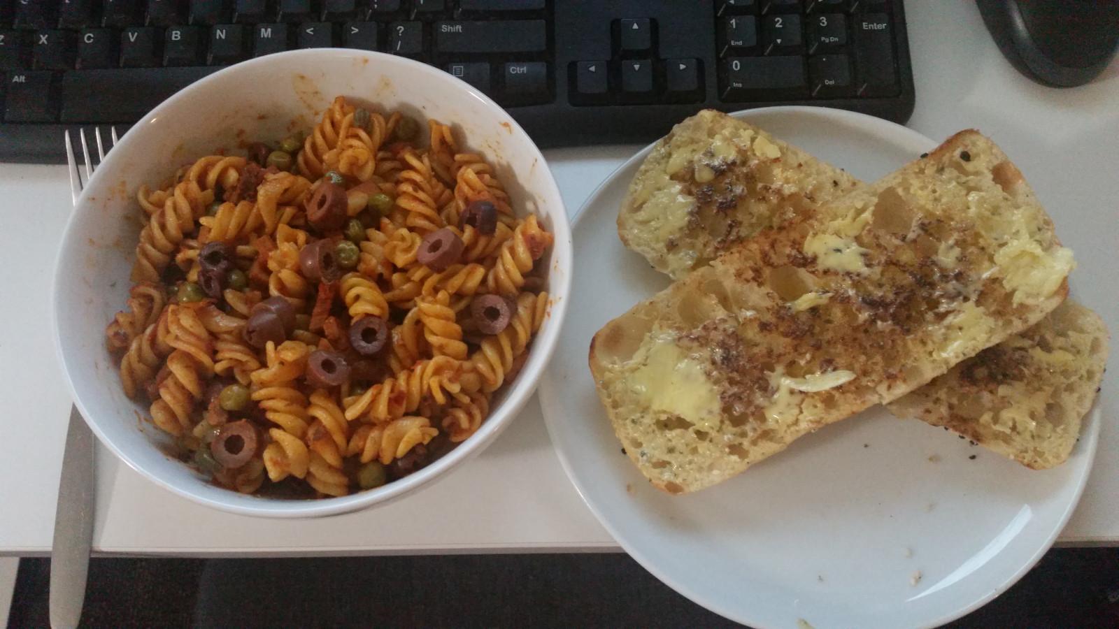 A bowl of reheated leftover pasta, complemented by two lightly toasted halves of a Turkish bread roll with garlic butter.