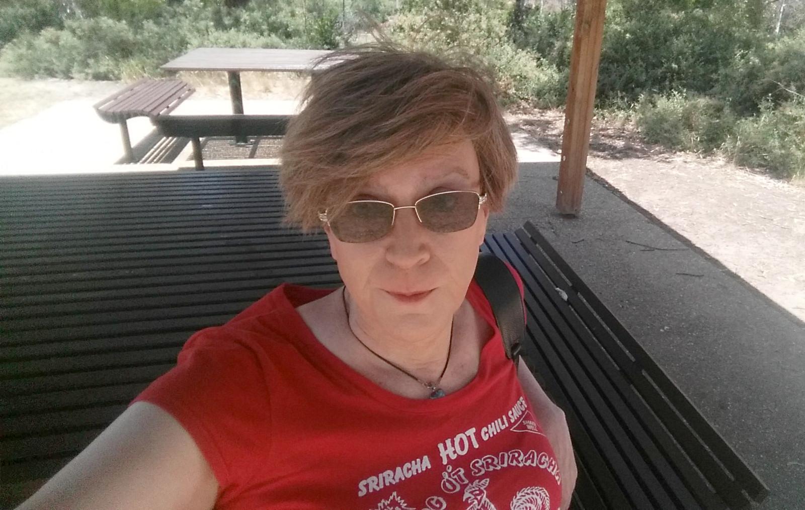 Old lady sitting at a table at a picnic area, looking worse for wear.